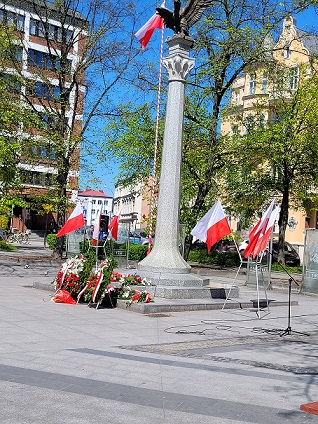 Pomnik Orła BIałego na Placu Konstytucji w Olsztynie oraz wieńce z biało- czerwonymi kwiatami.