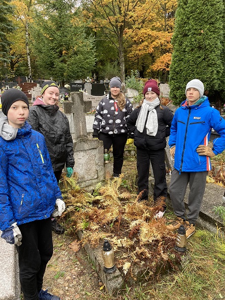 Wolontariusze stoją przy grobie na cmentarzu