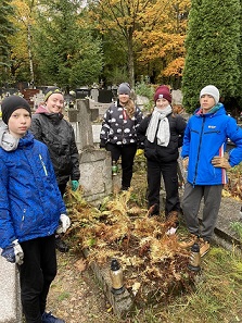 Wolontariusze porządkują zaniedbany grób na cmentarzu