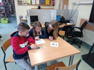 3-osobowe zespoły uczniów z klasy 3a siedzą przy stoliku, rozwiązując wspólnie zadania gramatyczno-ortograficzne na karcie pracy