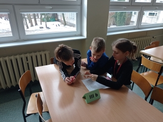 3-osobowe zespoły uczniów z klasy 3b siedzą przy stoliku, rozwiązując wspólnie zadania gramatyczno-ortograficzne na karcie pracy